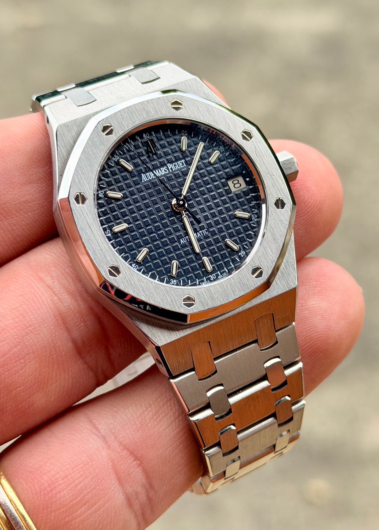 Silver watch with blue face held in a hand against a blurred background