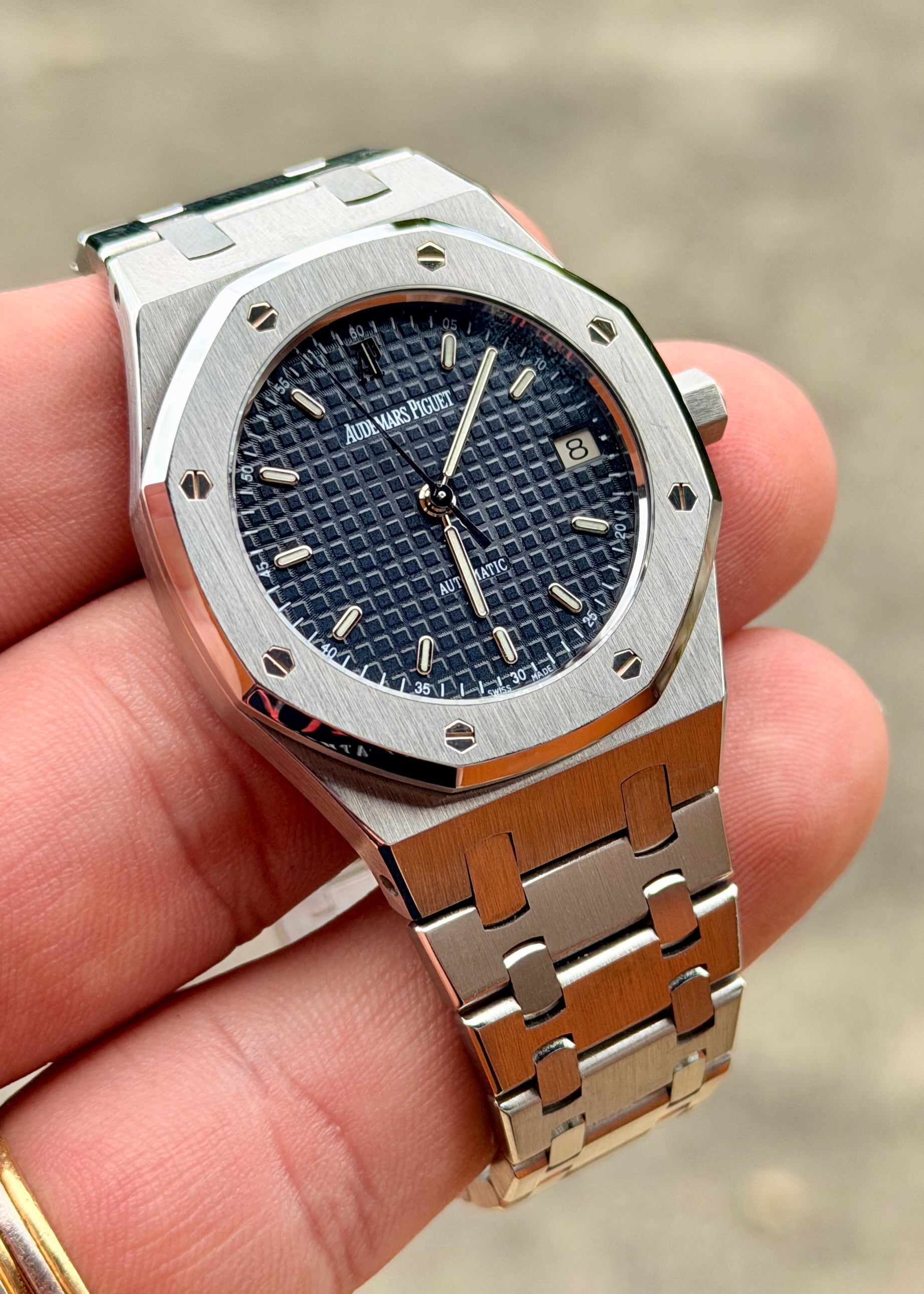 Silver watch with blue face held in a hand against a blurred background